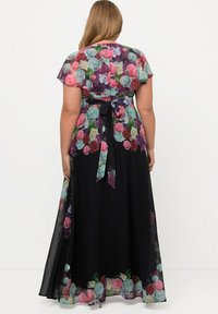 Robe maxi avec un imprimé floral dans des teintes de rose, violet et teal sur un fond noir. Manches transparentes et détail de taille nouée.