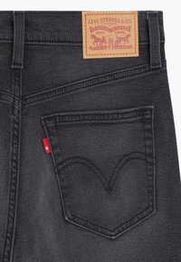 Poche arrière et écusson logo en cuir sur un jean en denim noir Levi Strauss montrant les coutures et une étiquette en tissu rouge.