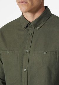 Camisa de botones verde oliva hecha de tejido suave, con cuello puntiagudo, dos bolsillos en el pecho y botones a juego.