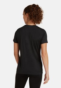 T-shirt nero a maniche corte con scollatura rotonda, texture morbida e dettagli sulla cucitura posteriore. Indossato con leggings neri.