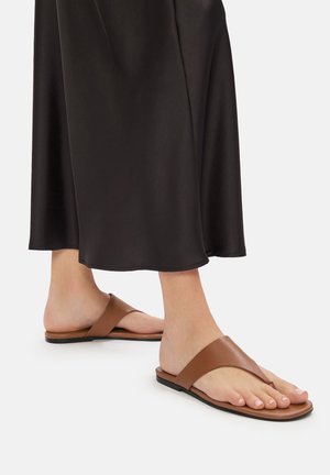 Hnědé ploché sandály s designem mezi prsty a širokými koženými popruhy, spárované s volnou černou saténovou sukní.