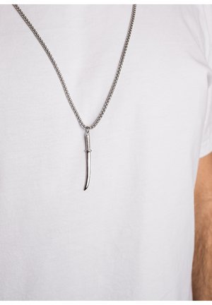 Silver chain necklace featuring a slender, curved pendant resembling a knife blade, set against a plain white shirt.