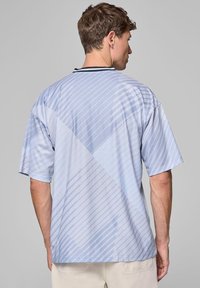 Koszulka z krótkim rękawem w jasnoniebieskim kolorze, z ukośnymi i poziomymi paskami o teksturowanym wykończeniu oraz czarnym detalem przy dekolcie.