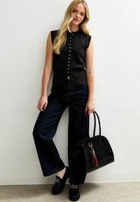 Svart ärmlös stickad topp med knäppning, parat med mörka vida jeans och svarta loafers. Accentaccessoarer inkluderar en texturerad svart handväska.