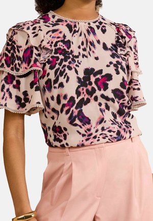 Camicia rosa con stampa leopardata viola e nera, maniche corte arricciate con rifinitura in pizzo, abbinata a pantaloni rosa pallido a vita alta e braccialetto dorato.