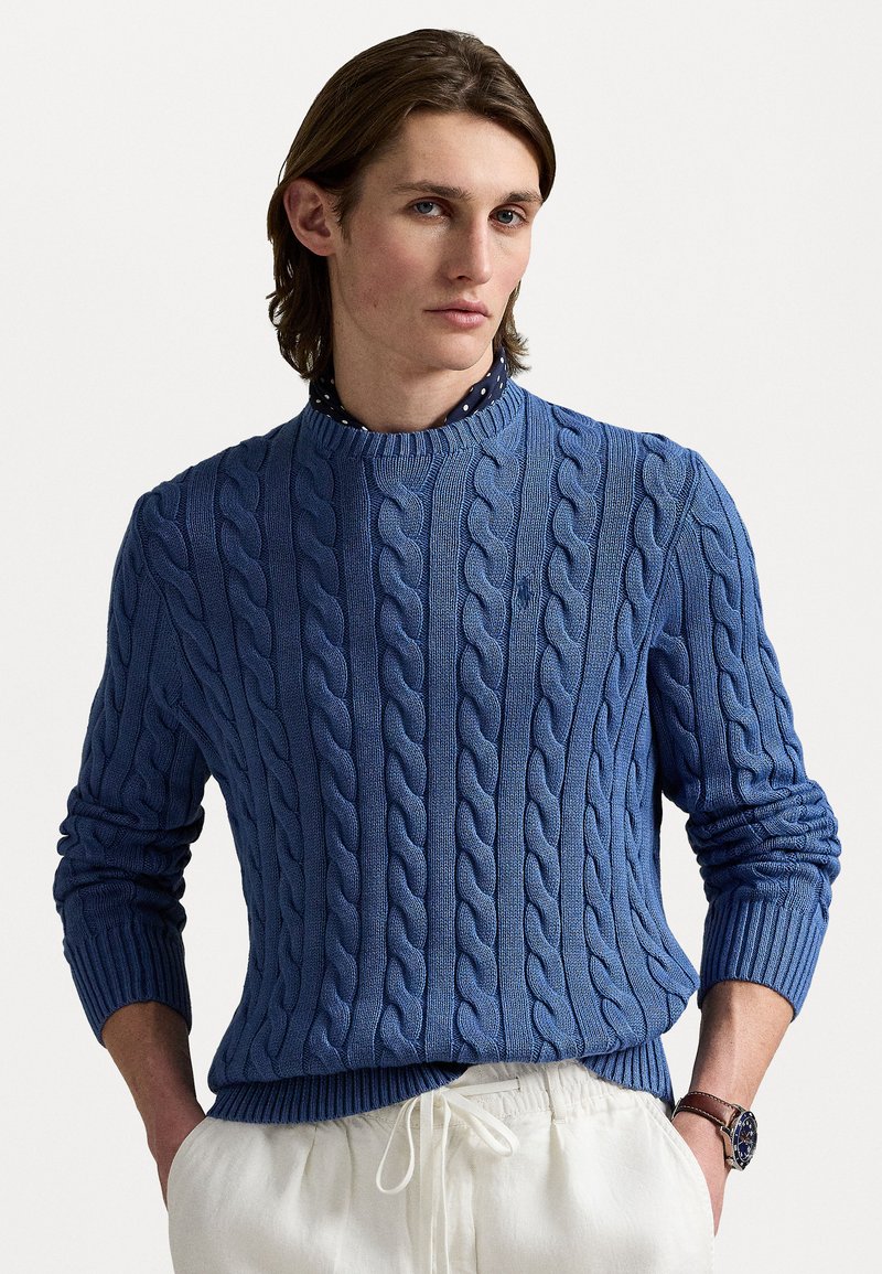 Lysblå kabelstrikket sweater med rund halsudskæring og ribbede manchetter. Båret med hvide bukser med snor og en prikket skjorte underneath.