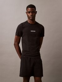 T-shirt atlético preto com design em rede e logótipo branco "CALVIN KLEIN" no peito, emparelhado com calções pretos combinando.