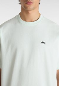 Hellgrün-mintfarbendes Baumwoll-T-Shirt mit Rundhalsausschnitt und kurzen Ärmeln. Auf der linken Brust befindet sich ein gesticktes schwarzes "VANS"-Logo.
