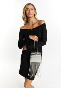 Hopeinen käsilaukku, jossa on geometrinen kuvio ja nauhakoristelu, valmistettu metallimateriaalista. Yhdistetty mustaan off-shoulder-mekkoon.