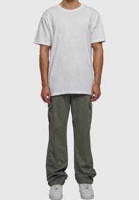 Biały bawełniany t-shirt z okrągłym dekoltem, zestawiony z luźnymi oliwkowozielonymi spodniami cargo z bocznymi kieszeniami i białymi trampekami.