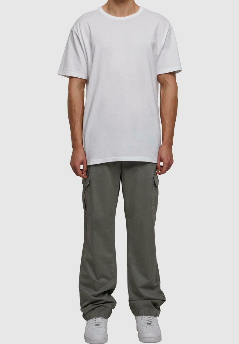 Biały bawełniany t-shirt z okrągłym dekoltem, zestawiony z luźnymi oliwkowozielonymi spodniami cargo z bocznymi kieszeniami i białymi trampekami.