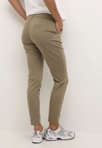 Beżowe spodnie o dopasowanym kroju z kieszeniami, slim fit i skróconą długością, w zestawie z szaro-białymi sneakersami. Gładka tekstura, brak widocznych wzorów.