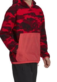 Röd och svart mönstrad fleece-hoodie med en kontrasterande röd nylonframficka och justerbar fåll, med huva och långa ärmar.