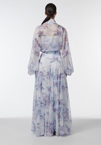 Mujer de espaldas a la cámara, con un vestido transparente, de manga larga y hasta el suelo, con estampado de acuarela en tonos pastel.