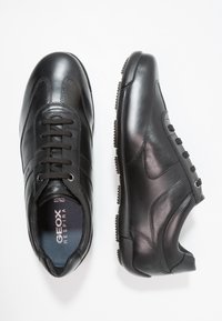 Baskets en cuir noir à texture lisse, dotées de six œillets, d'un bout rond et d'une semelle en caoutchouc à motif pour une meilleure adhérence. Marque Geox visible.
