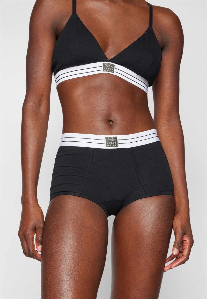 Bralette preta com um design triangular e alças ajustáveis; cuecas de cintura alta pretas a condizer, com uma cintura riscada em branco.