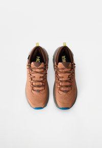 Chaussures de randonnée marron avec accents gris, empeigne texturée, design à lacets et petites languettes jaunes. Semelle extérieure en caoutchouc bleue.