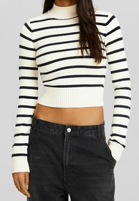 Kort tröja i krämfärg med marinblå horisontella ränder, med ribbat halsringning och muddar, kombinerad med svarta jeans med hög midja.