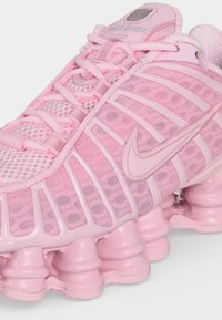 Κοντινό πλάνο ροζ αθλητικού παπουτσιού Nike Shox που δείχνει το πλεκτό επάνω μέρος, μοναδική τμηματική σόλα και το λογότυπο Nike swoosh στο πλάι.