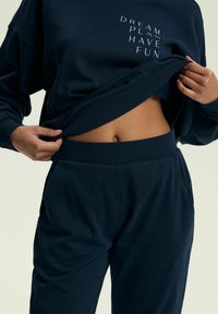 Granatowa bluza z białym napisem "MARZ, PLANUJ, MIEJ FRAJDĘ" w zestawie z dopasowanymi dresami z dzianinowym paskiem w pasie i bocznymi kieszeniami.