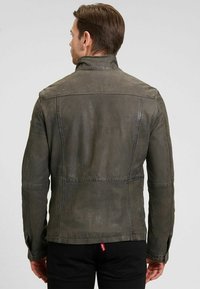 Graue Lederjacke mit hohem Kragen, sichtbaren Nähten und matter Textur. Die Rückseite zeigt ein tailliertes Design und subtile Akzente.