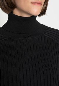 Pull noir à col roulé avec texture côtelée verticale et coupe ajustée. Tissu lisse avec un col haut et des accents aux épaules.