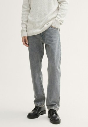 Light blue denim jeans with a straight leg fit, featuring faded areas and classic five-pocket design, paired with black lace-up shoes.