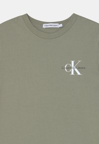 Oliwkowa bawełniana koszulka z okrągłym dekoltem, z białym logo, które głosi "Calvin Klein Jeans" oraz wyraźnymi literami "CK".