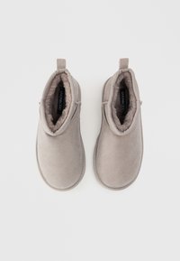 Botas de tornozelo em suede cinza com um interior forrado suave, design slip-on, bordas cosidas e puxador traseiro. Textura suave com detalhes mínimos.
