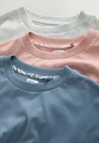 Trois t-shirts à col rond empilés : gris clair, rose doux et bleu sarcelle, avec des cols côtelés et un détail floral à l'intérieur du col.