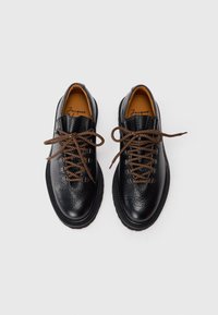 Black leather shoes with a textured finish, brown laces, and metal eyelets, featuring a rounded toe and thick rubber soles.