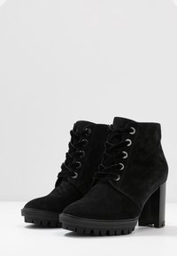 Bottines en suede noir avec un talon épais, un devant à lacets, des œillets en métal et une semelle en caoutchouc texturé présentant un motif de semelle.