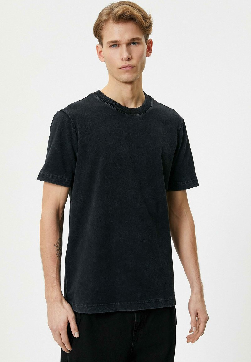 Camiseta de algodón negra con un escote redondo, mangas cortas y una textura ligeramente desgastada. Presenta costuras visibles y un corte relajado.