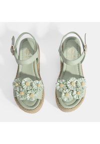 Grüne Leder-Sandalen mit Espadrille-Sohlen, verziert mit Stoffblumen und Strohmittelpunkten. Verstellbarer Knöchelriemen mit metallischen Beschlägen.