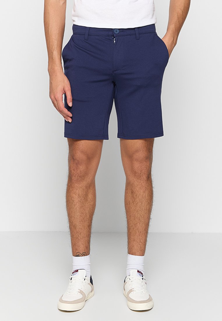 Navy blue shorts made of soft fabric, featuring a classic fit, front pockets, a button closure, and styled with white sneakers.