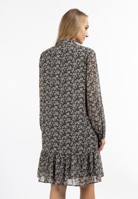Rochie florală de culoare neagră cu mâneci lungi dintr-un material transparent, tiv fluturat și corset ajustat. Prezintă o guler mic și un model floral dens în tonuri atenuate.