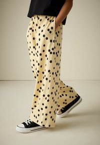 Pantalones culottes amarillos con lunares negros, con un ajuste relajado y bolsillos laterales, combinados con zapatillas negras de corte bajo.