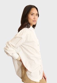 Crème kleurig overhemd met knoopsluiting, met een puntige kraag, lange mouwen en een relaxte pasvorm. Bevat een enkele borstzak en knoopaccenten.