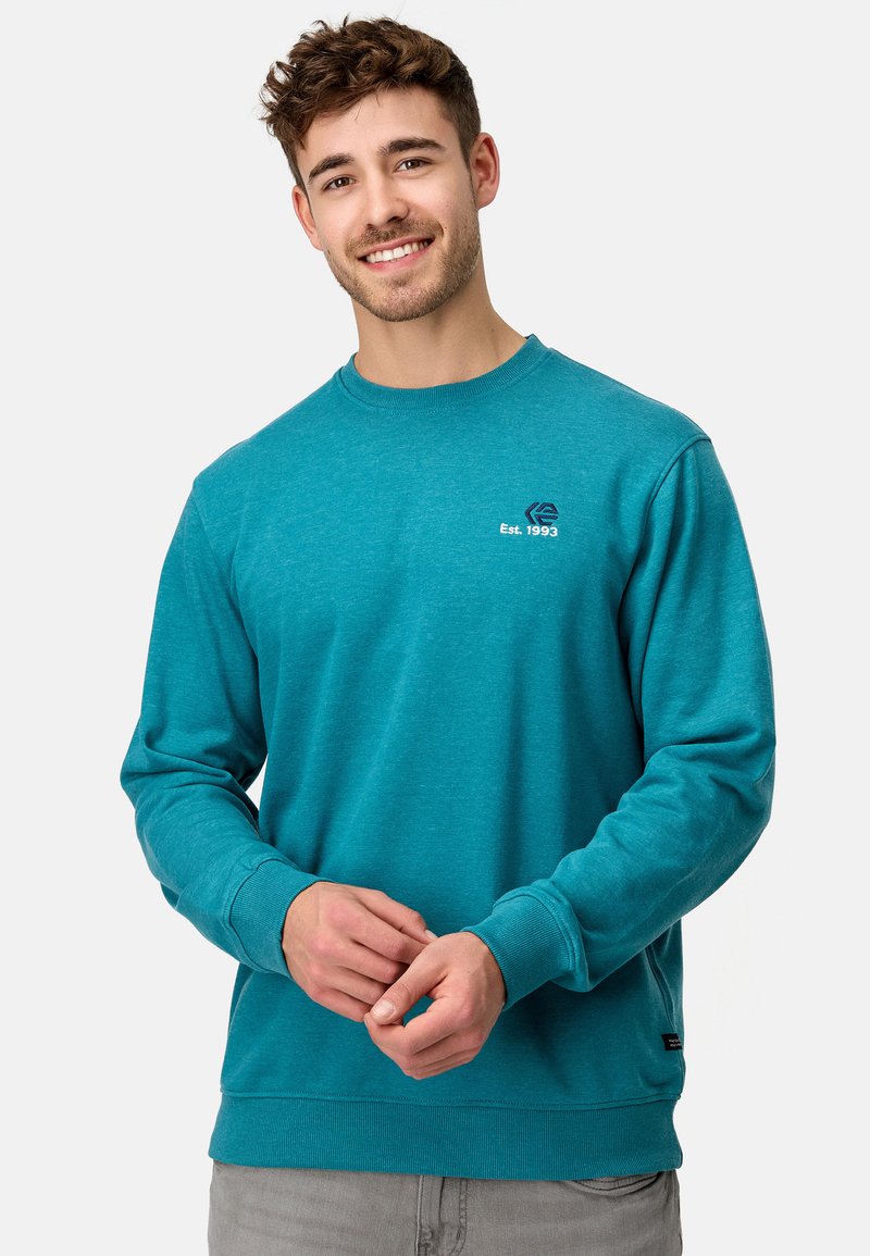 Teal sweatshirts, van een katoenmix, ronde hals, ribgebreide manchetten en onderrand. Logo op de linkerborst met "Est. 1993" in wit en donkerblauwe stiksels.