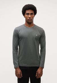 T-shirt a maniche lunghe in tessuto grigio scuro con colletto a girocollo e un piccolo logo sul petto. Tessuto liscio, design aderente, senza fantasie.