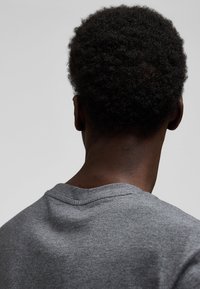 Mies, jolla on lyhyet kiharat hiukset ja harmaa pyöreäkauluksinen paita, esitetty takaapäin yksinkertaisen vaalean taustan edessä.