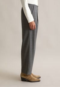 Grijze geblokte broek met een relaxte pasvorm, voorzien van plooien en zijzakken, gecombineerd met beigekleurige enkellaarsjes en een wit langemouwen top.