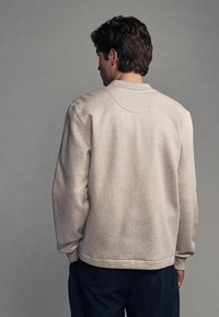 Hanorac gri deschis, cu guler rotund și mansete ribelate. Textură moale, design pătrățos și o croială ușor relaxată. Stil clasic.