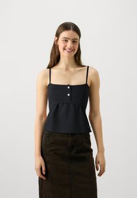 Svart ribbet crop top med tynne stropper, med knappelukking og peplumkant, kombinert med et mørkt denimskjørt.