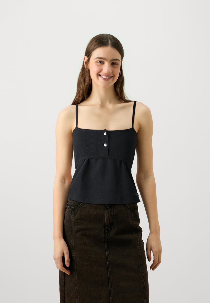 Svart ribbet crop top med tynne stropper, med knappelukking og peplumkant, kombinert med et mørkt denimskjørt.