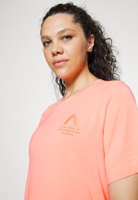T-shirt rosa claro de mangas curtas, decote redondo, e texto impresso: "SER GRANDE EM QUALQUER COISA REQUER PACIÊNCIA" em fonte laranja.