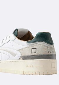Witte sneakers met groene hielinleg, beige en grijze suede accenten, embossed "D.A.T.E." op de zool en gestikte vierkante logo op de zijkant.
