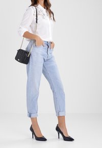 Camicia bianca con dettagli in pizzo, jeans azzurri arrotolati, borsa nera trapuntata e scarpe nere con tacco alto.