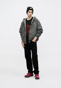 Chaqueta acolchada gris con capucha, camiseta gráfica negra, jeans negros y zapatillas deportivas rosas. Los accesorios incluyen un gorro negro.