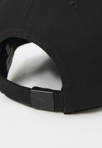 Casquette de baseball noire avec une visière incurvée, un tissu texturé, une sangle ajustable dotée d'un fermoir en métal noir et des détails de logo discrets.